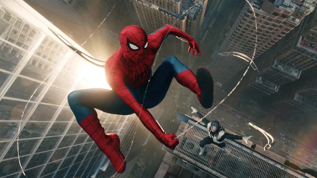 A superhero wearing a red and blue costume with a spider emblem swings through the air above a city skyline, with buildings and a person in black and white below.